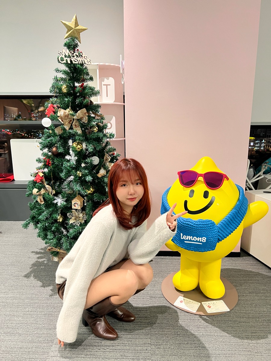 Me crouching beside the Lemon8 mascot next to the office Christmas tree