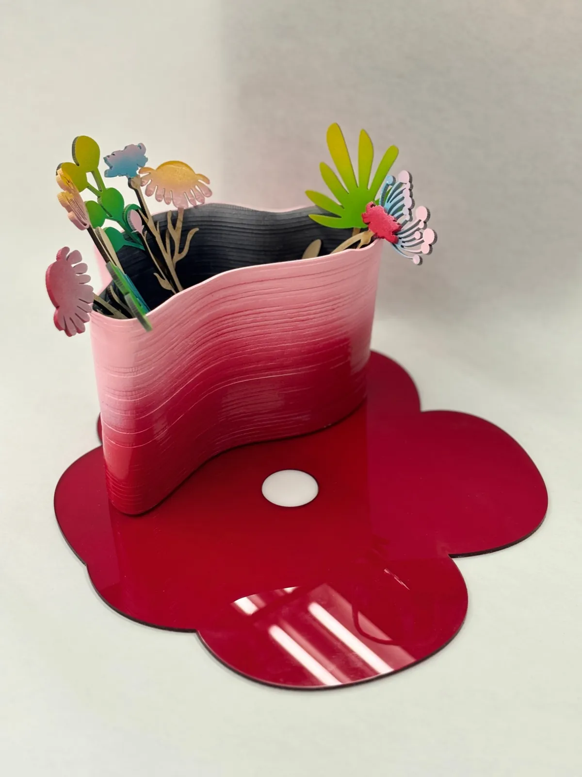 Pink wavy vase of laser-cut, spray-painted wooden flowers on a red flower-shaped base
